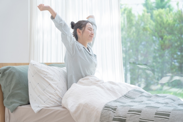 朝、ベッドの上で両腕を伸ばしてストレッチする女性